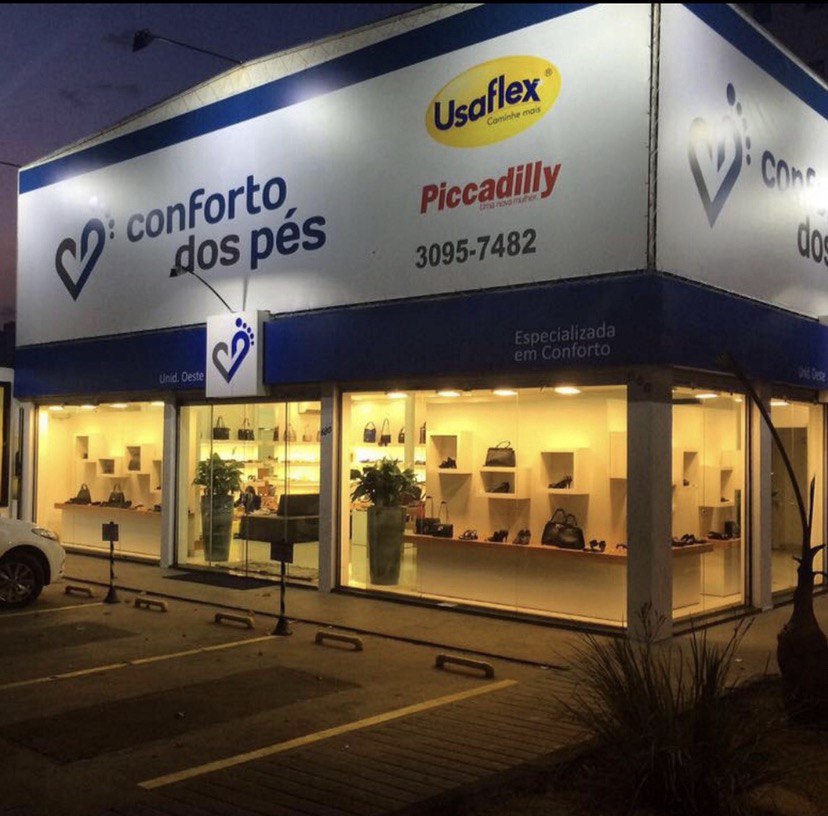 Fachada iluminada da loja Conforto dos Pés do Setor Oeste em Goiânia, com vitrines de calçados femininos e bolsas